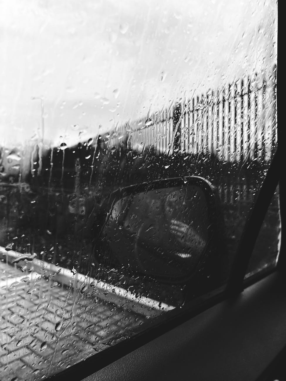 wet car window and rear viewer covered with raindrops